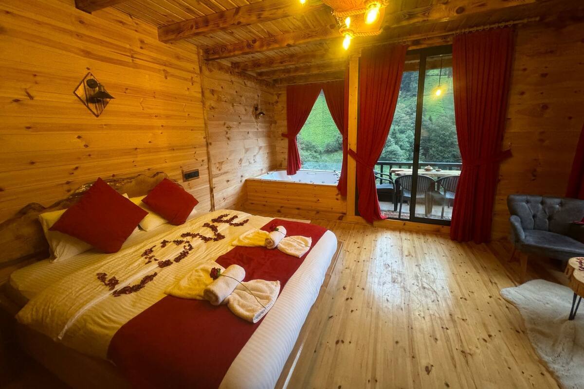 Une chambre aménagée dans une cabane en bois, avec un lit, des rideaux rouges et une vue sur l’extérieur.
