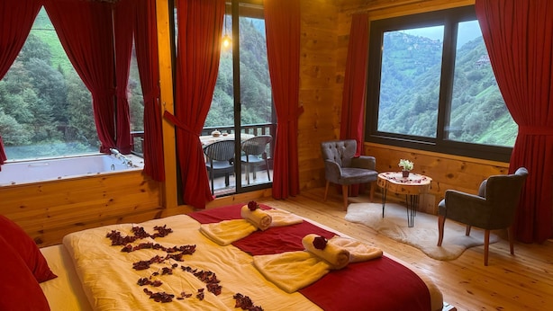 Una habitación de cabaña de madera con una cama grande, cortinas rojas y vistas a un paisaje boscoso.