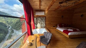 Una cabaña de madera con cama, sofá, mesa y vistas a un río y montañas.