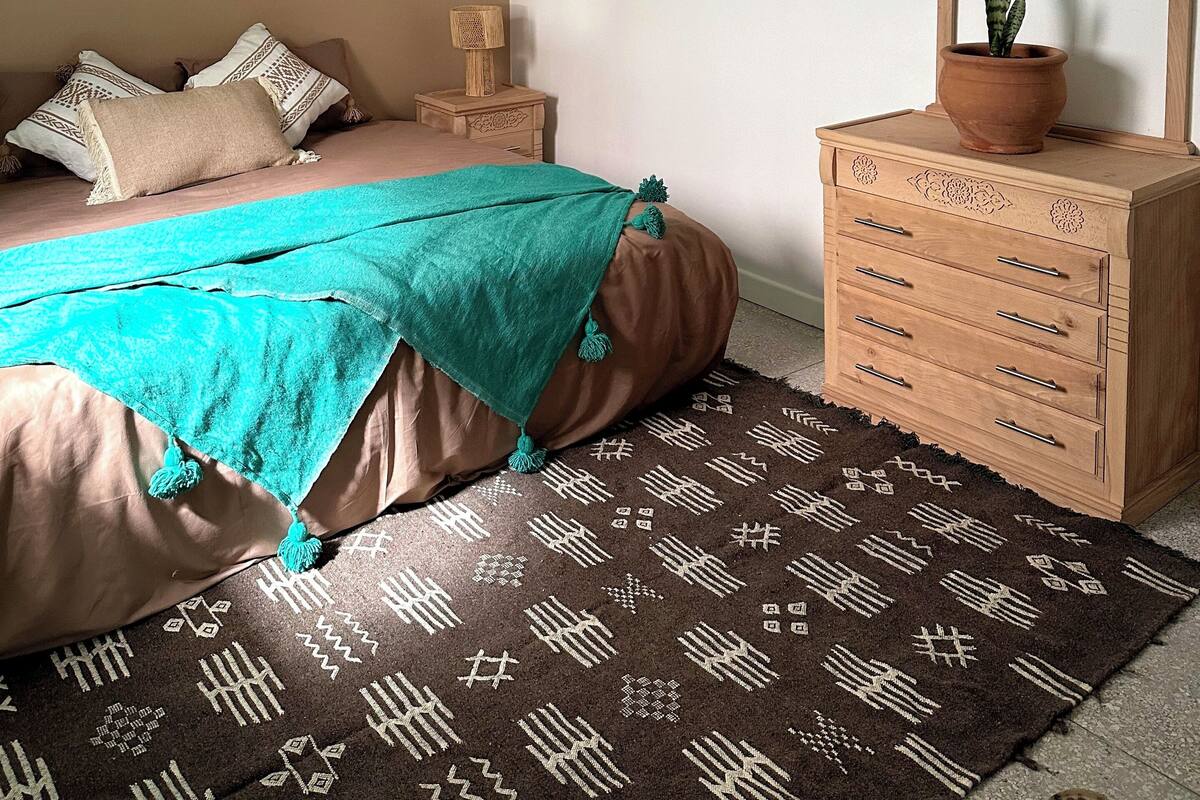 A bedroom with a bed, a dresser, a mirror, a hanging lamp, and a patterned rug.