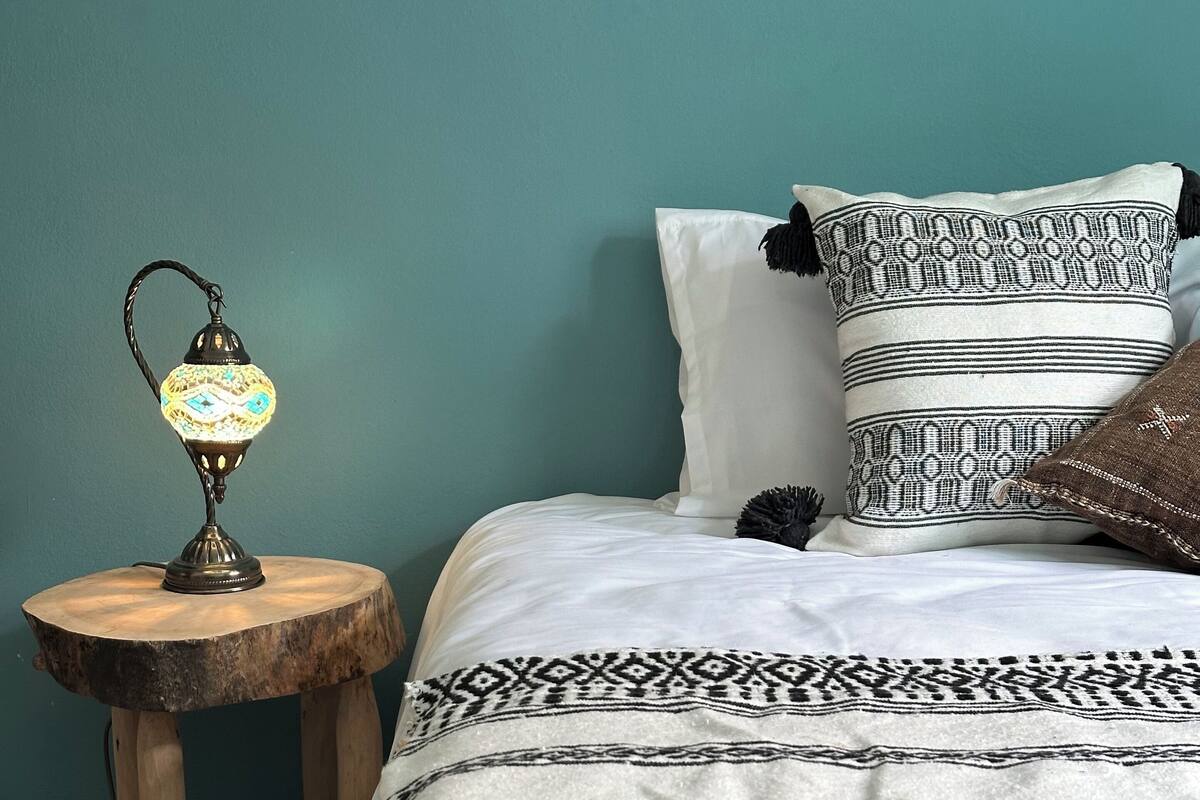 A bed with patterned bedding, a nightstand with a lamp, and a teal wall.