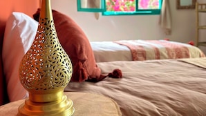 A room with a bed, a window with curtains, a mirror, and a decorative lamp on a wooden table. - Dar Al-Andalus (Tamraght)