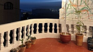 A balcony with terracotta tiles, white balustrade, potted plants, and a view of the city at dusk. - Dar Al-Andalus (Tamraght)