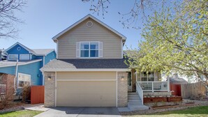 A two-story house with a beige garage door, a small porch with a white railing, and a brick foundation. - 17 Mi to Dtwn Denver: Family Home w/ Private Yard (Commerce City)