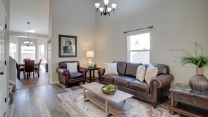 A spacious living room with a brown leather sofa, a wooden coffee table, and a chandelier. - 17 Mi to Dtwn Denver: Family Home w/ Private Yard (Commerce City)