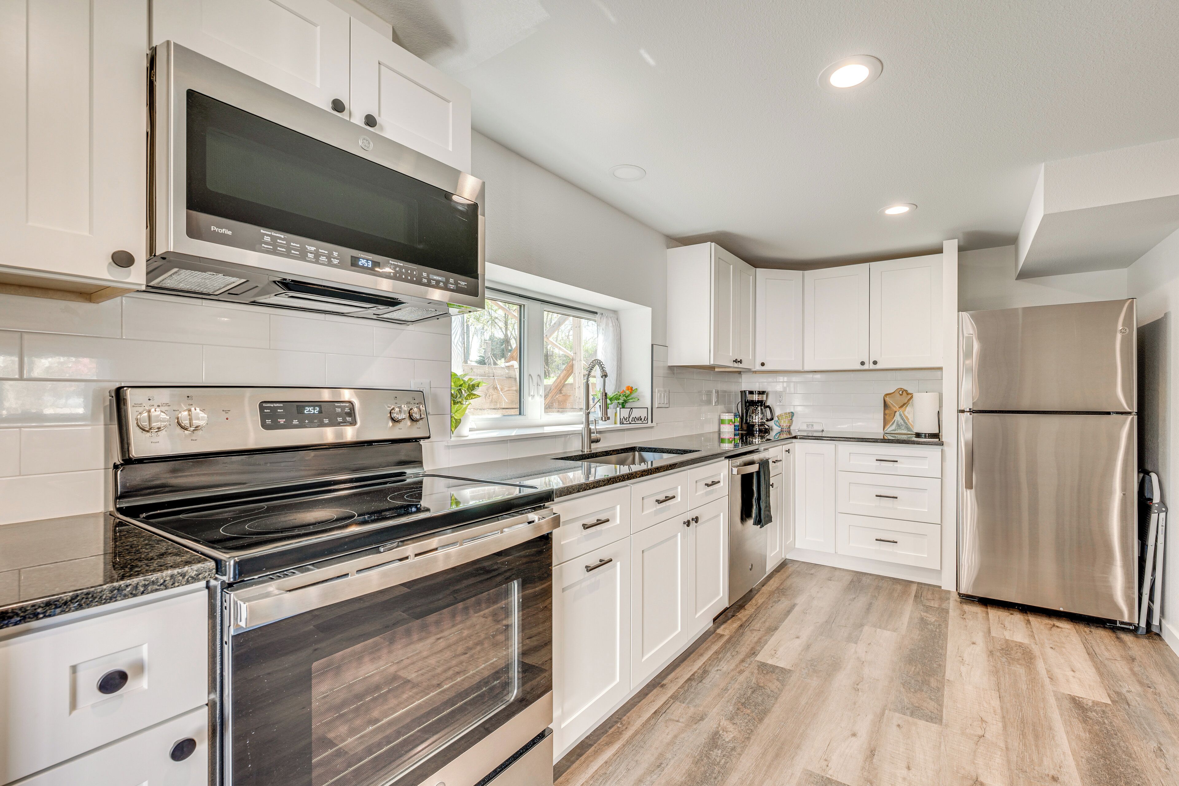 A modern kitchen with white cabinets, stainless steel appliances, and a herringbone wood floor.