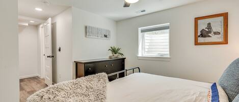 A bedroom with a bed, a ceiling fan, a window, a dresser, and a framed picture on the wall.