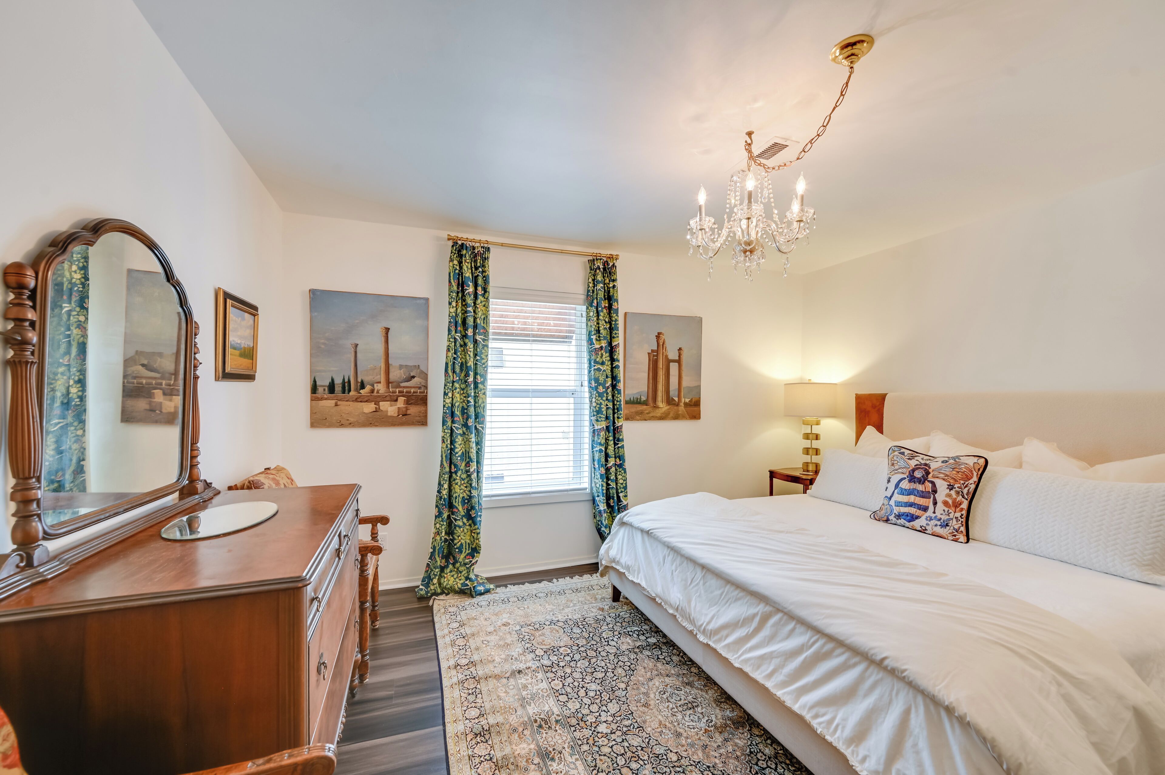 A bedroom with a large bed, a dresser, a mirror, and a chandelier.