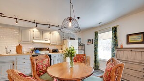 Una cocina con armarios blancos, una mesa de comedor de madera con sillas y una lámpara colgante.