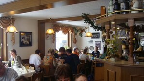 L’intérieur d’un restaurant est aménagé avec des meubles en bois, des lampes suspendues et un coin bar où sont exposées des bouteilles.