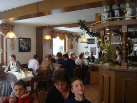 Interior de restaurante com móveis de madeira, luminárias pendentes e área de bar com garrafas.