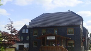 Un bâtiment à deux étages, doté d’un toit sombre et d’un porche en bois. Une enseigne au-dessus de l’entrée indique : « Gasthof & Pension Kemter ».