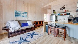 A modern kitchen with wooden cabinets, a bar area, and a seating area with a sofa and a starfish rug. - Beachfront Retreat w/ Dock in Lanark Village! (Carrabelle)