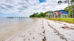 A beach with a wooden pier extending into calm waters, surrounded by colorful houses with balconies. - Beachfront Retreat w/ Dock in Lanark Village! (Carrabelle)