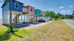 A beachfront property with three colorful houses elevated on stilts, a sandy path, and a road curving to the right. - Beachfront Retreat w/ Dock in Lanark Village! (Carrabelle)