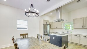 Une cuisine moderne avec des meubles blancs, un îlot central et un coin repas comprenant une table et des chaises en bois.
