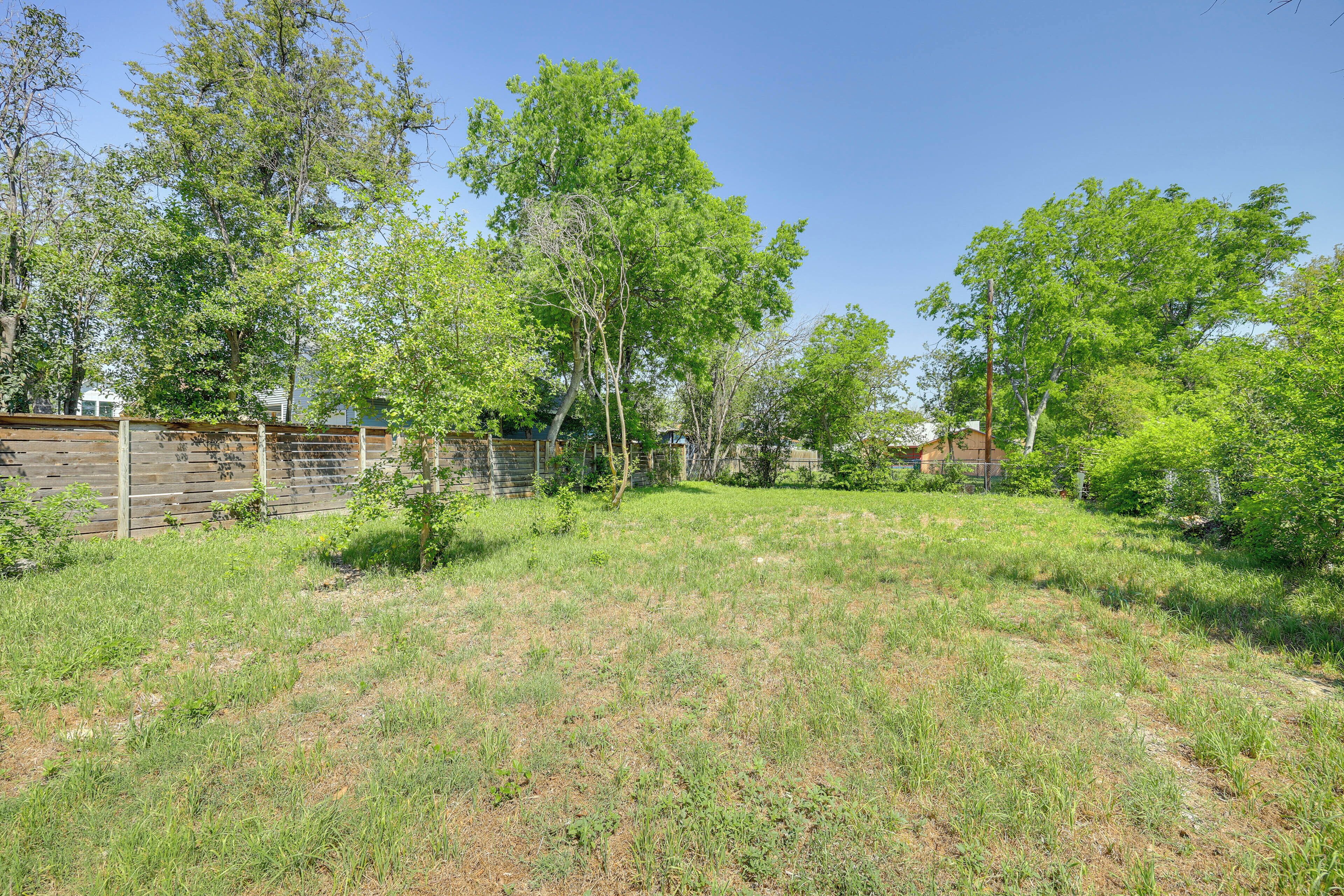 A backyard with a wooden fence, trees, and a grassy lawn.