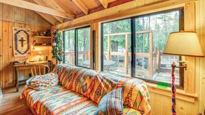 A cozy cabin interior with a wooden ceiling, a large window with a view of the outdoors, a colorful sofa, and a lamp. - 4 Mi to Lake Tahoe: Cozy Cabin w/ Deck! (South Lake Tahoe)