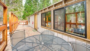 A wooden deck with metal tables and chairs, large windows, and a view of a forest. - 4 Mi to Lake Tahoe: Cozy Cabin w/ Deck! (South Lake Tahoe)
