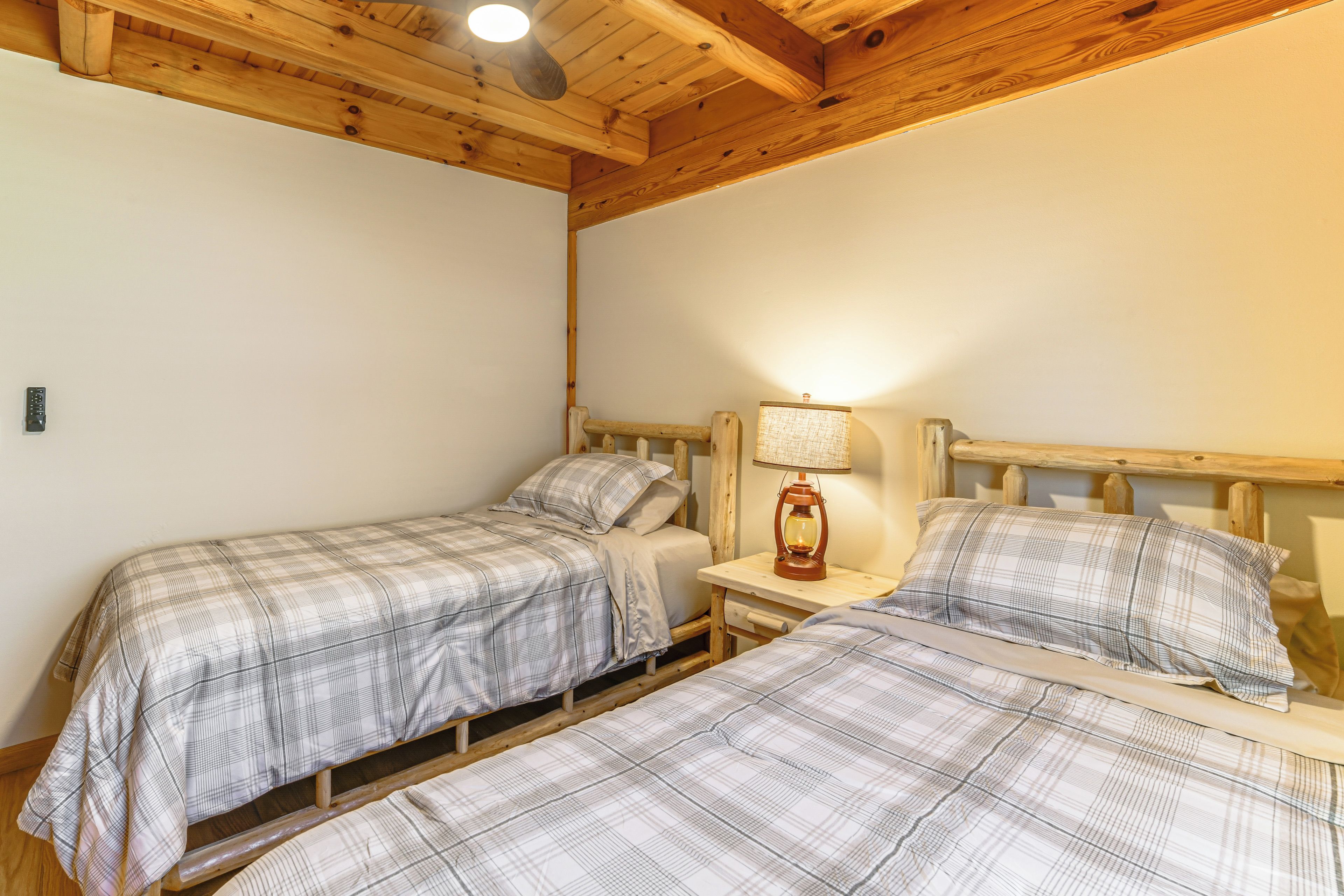A bedroom with two beds, wooden headboards, a nightstand with a lamp, and a ceiling light.