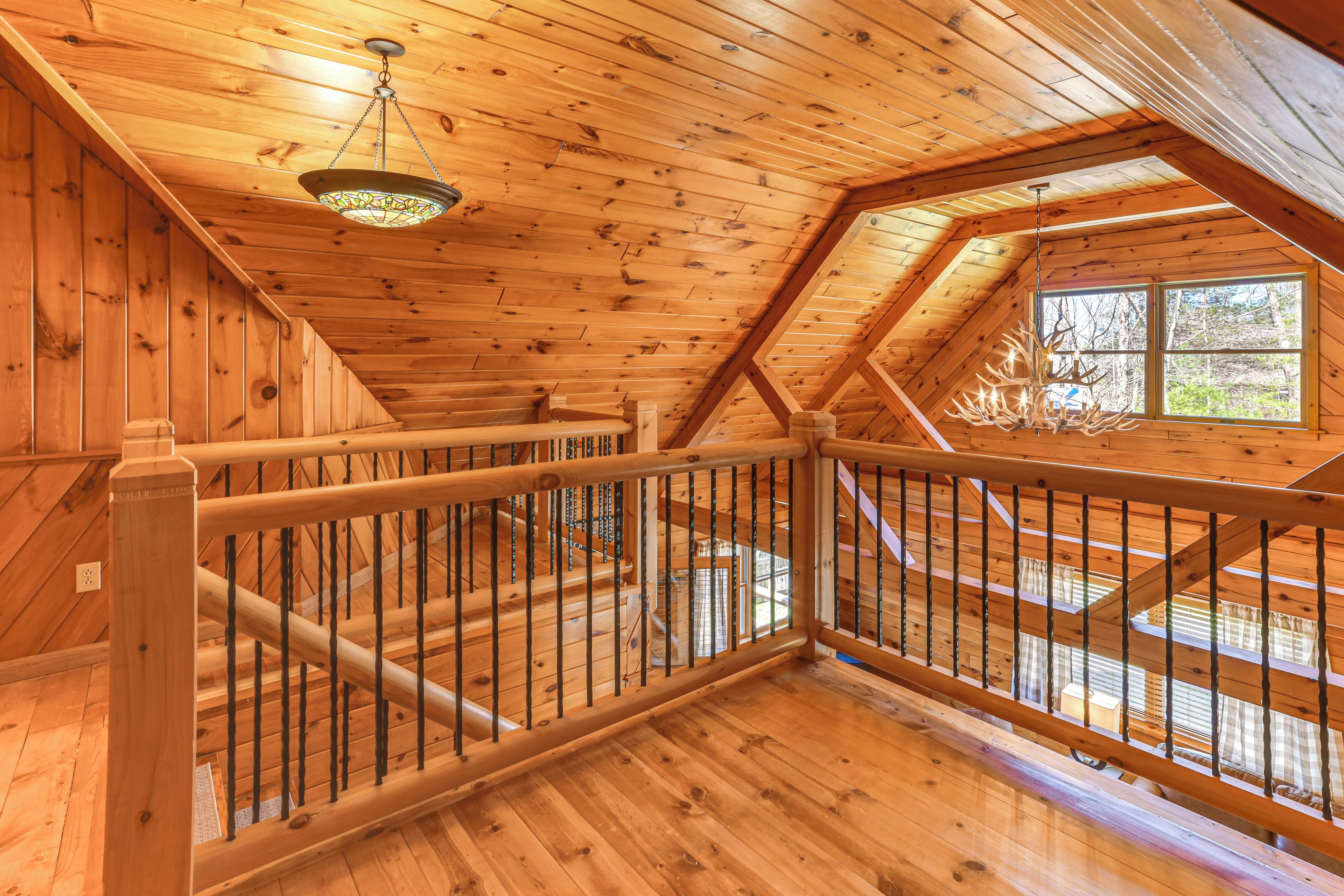 Interior de madera con una escalera, barandillas de madera y un ventanal grande.