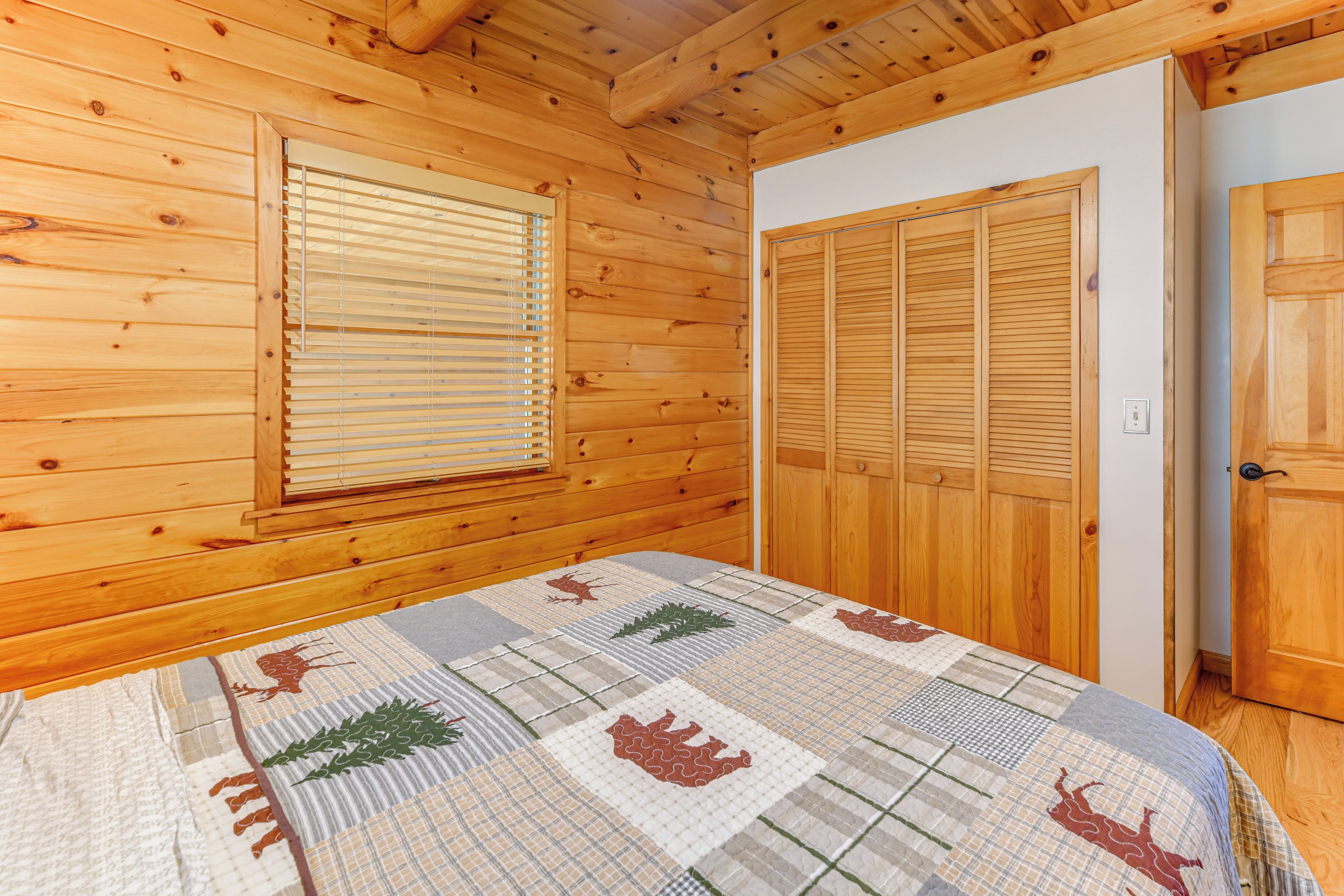 A wooden cabin room with a bed, a window with blinds, and a set of wooden closets.