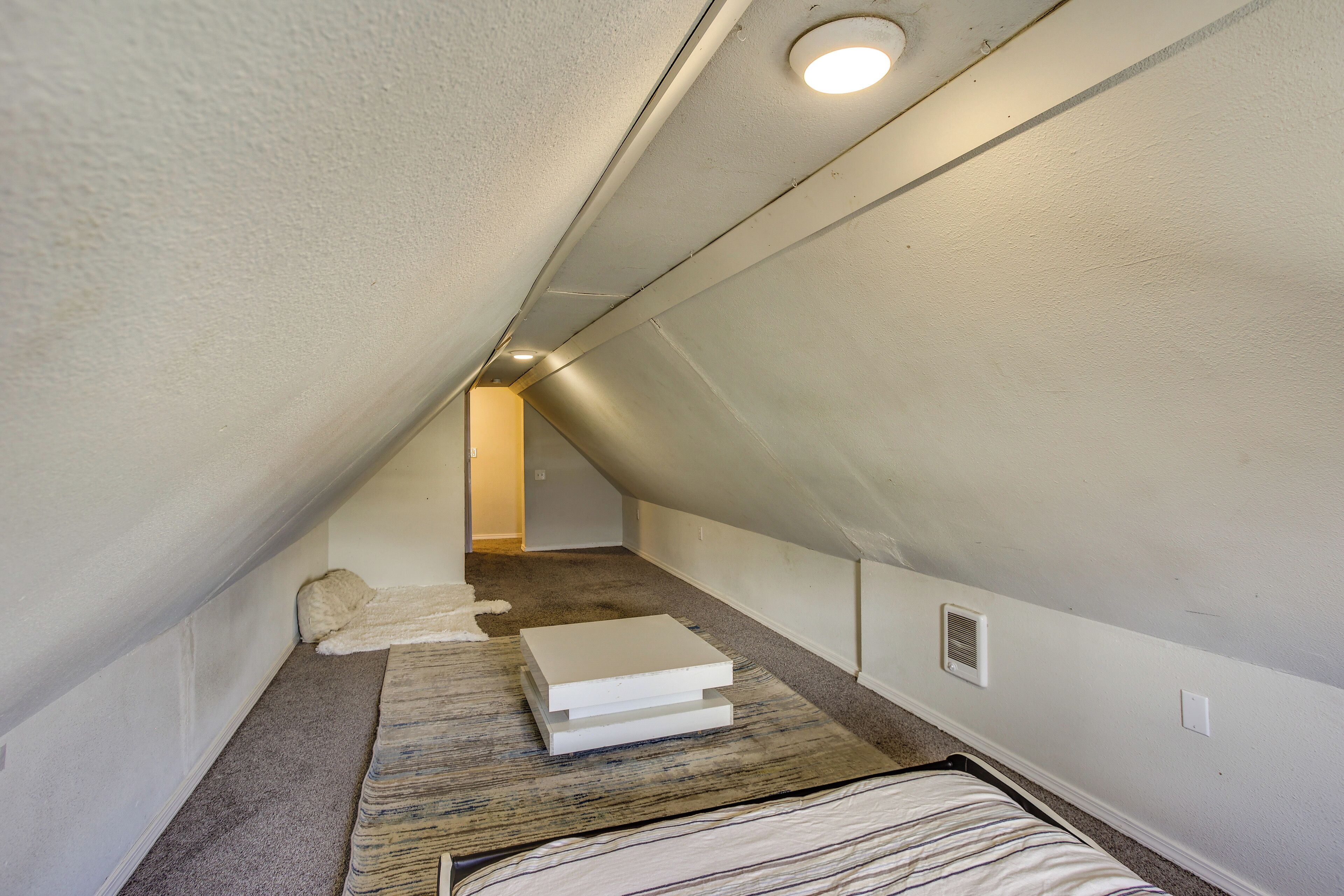 A narrow attic room with a sloped ceiling, a small window, and a radiator.