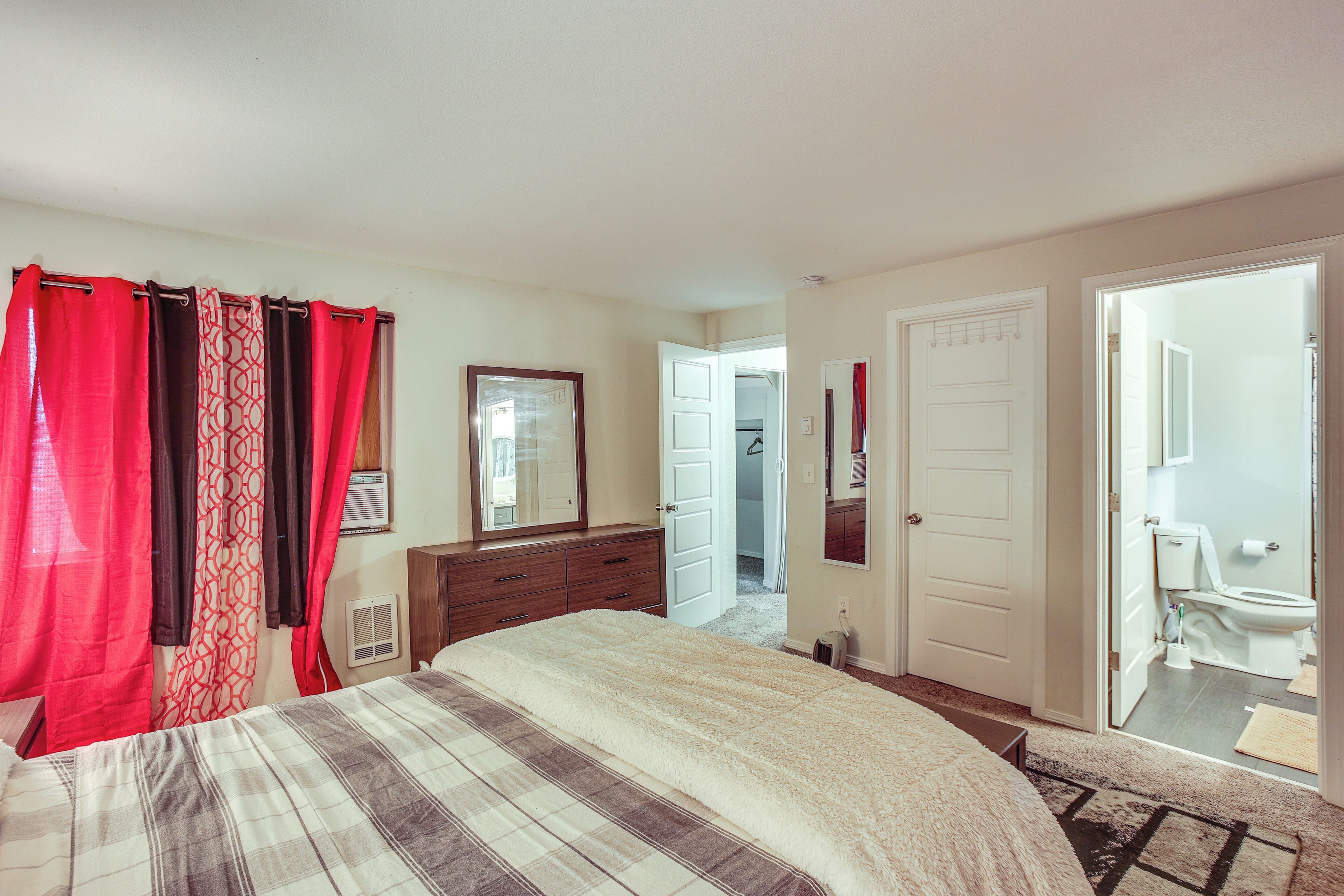 A bedroom with a bed, a dresser, a mirror, and a door leading to a bathroom.