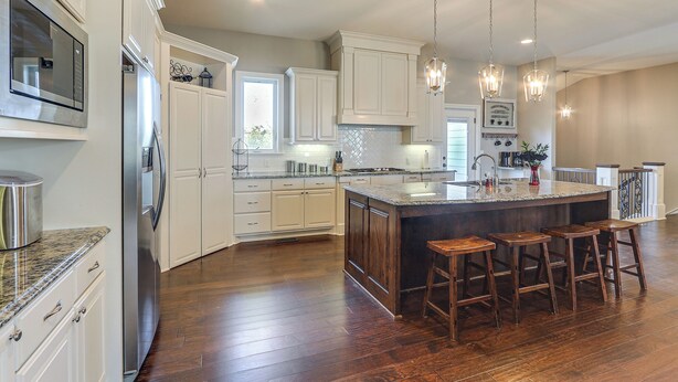 A spacious kitchen with white cabinetry, a large island with bar stools, stainless steel appliances, and pendant lighting. - Balcony & Patio: Spacious Home in Bel Aire! (Wichita)