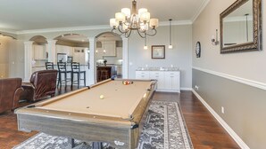 A spacious living area with a pool table, a dining area with chairs, and a kitchen in the background. - Balcony & Patio: Spacious Home in Bel Aire! (Wichita)