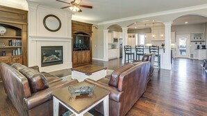 A spacious living room with leather sofas, a fireplace, and a kitchen in the background. - Balcony & Patio: Spacious Home in Bel Aire! (Wichita)