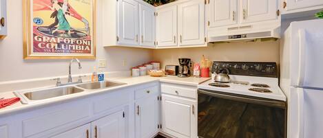 A kitchen with white cabinets, a sink, a stove, and a refrigerator.