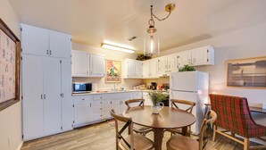 A compact kitchen with white cabinets, a dining table with chairs, and a hanging light fixture. - 2 Mi to Bitterroot River: Downtown Corvallis Apt! (Corvallis)
