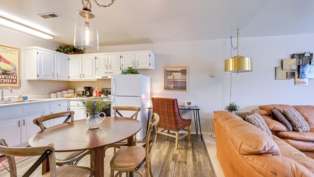 A modern kitchen with white cabinets, a dining table with chairs, a refrigerator, and a hanging light fixture. - 2 Mi to Bitterroot River: Downtown Corvallis Apt! (Corvallis)