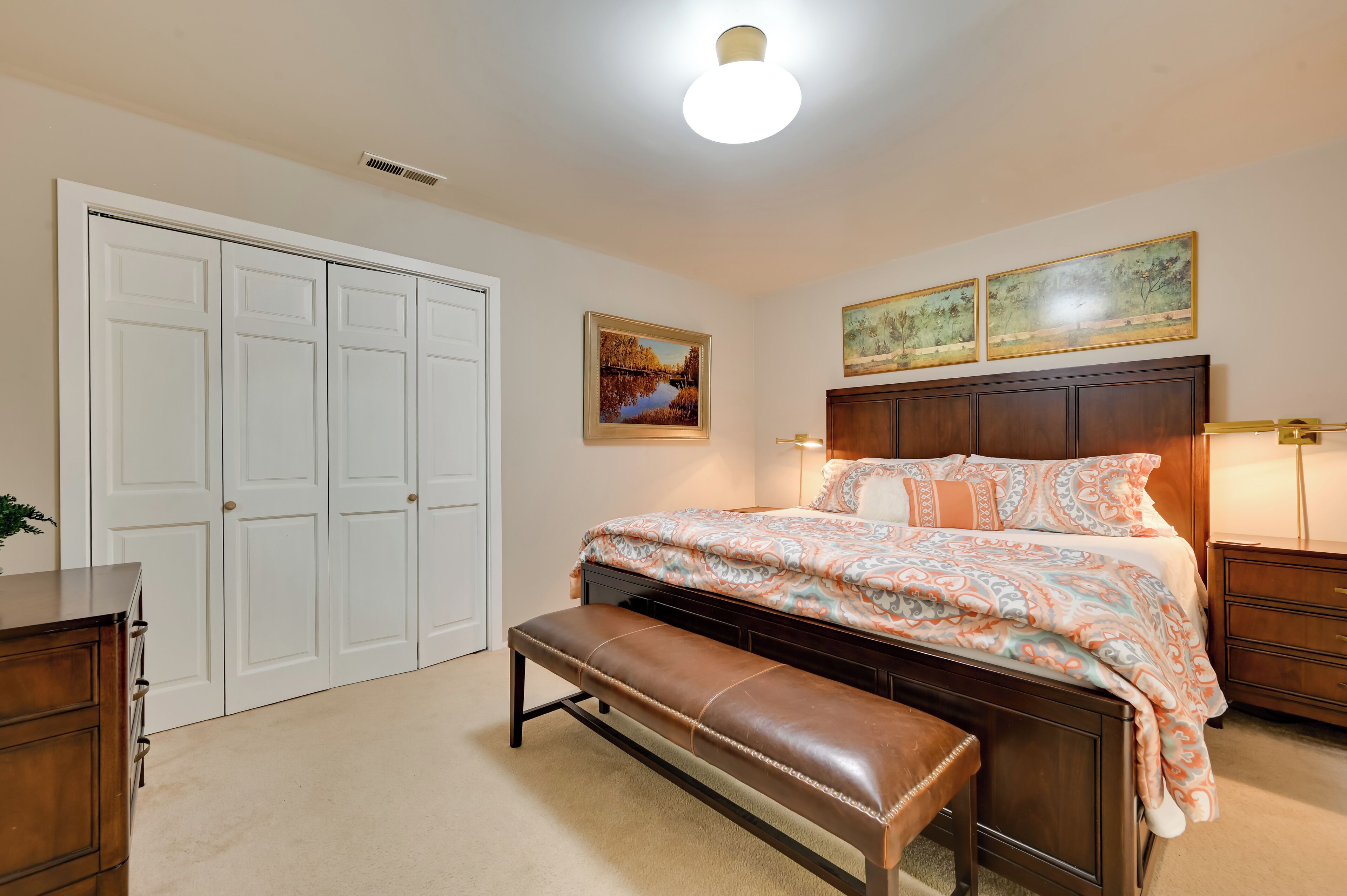 A bedroom with a large bed, a bench, a dresser, a wardrobe, and two wall-mounted lamps.