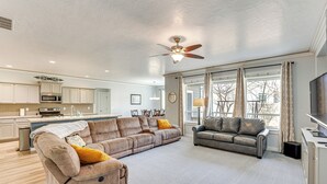A spacious living room with a large sectional sofa, a smaller sofa, and a grey leather couch. There is a ceiling fan, a flat-screen TV, and a kitchen in the background. - Kuna Group Getaway w/ Patio & Grill (Kuna)