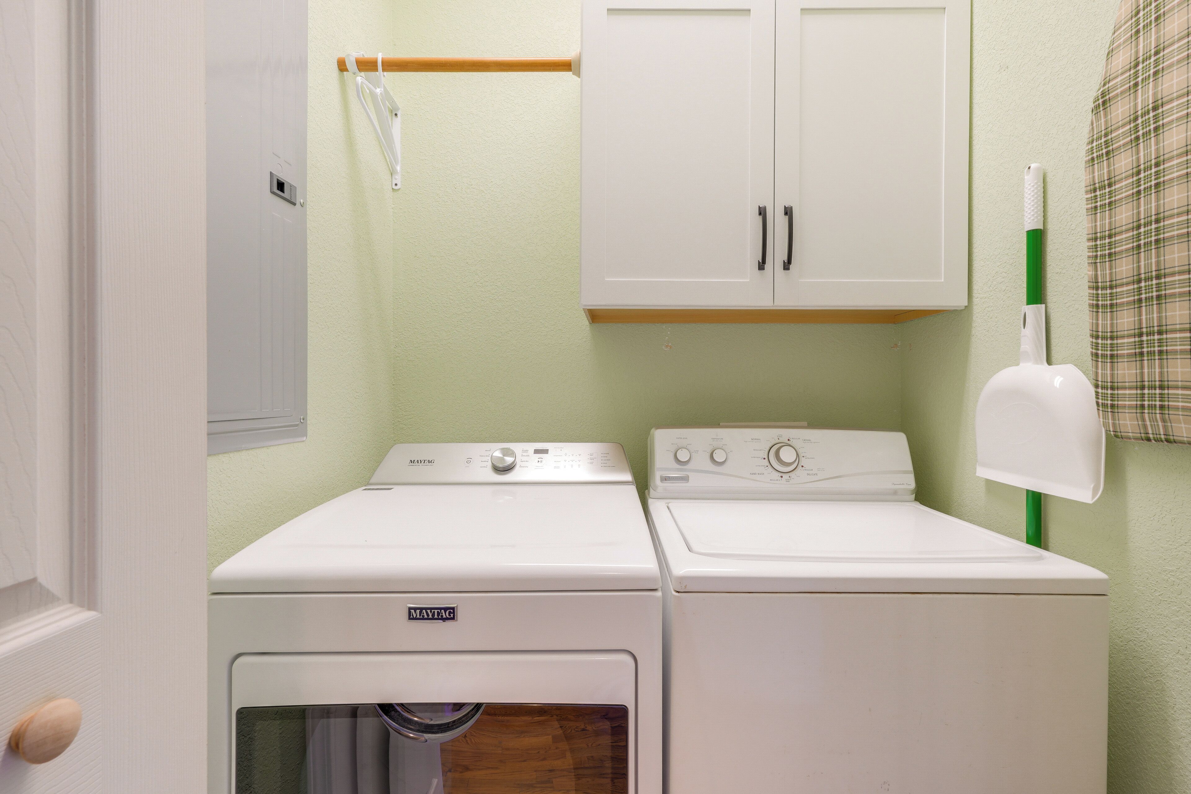 Un cuarto de lavado con dos lavadoras y secadoras Maytag blancas, una puerta de madera y una pared verde.