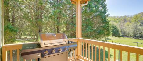 A covered outdoor area with a barbecue grill, wooden deck, and a view of a forested landscape.