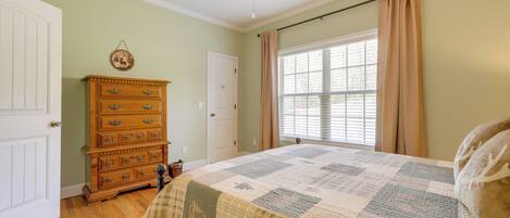 A bedroom with a wooden dresser, a quilted bedspread, a ceiling fan, and a window with curtains.