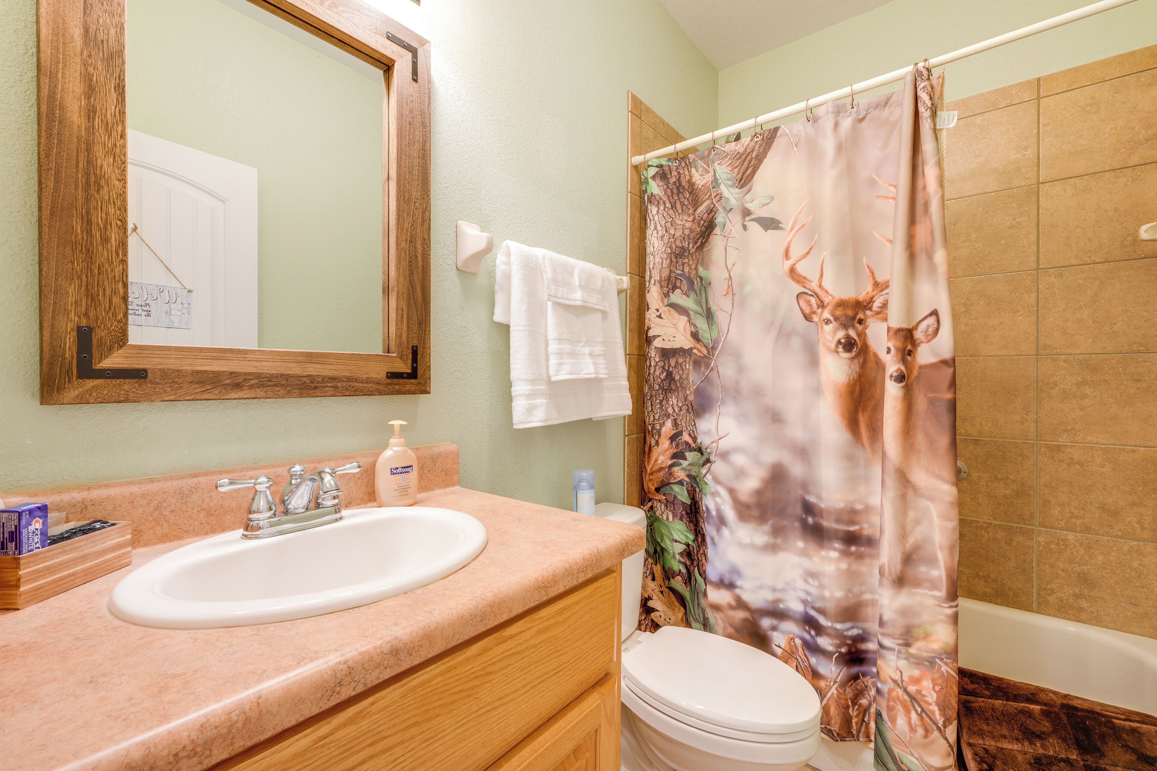 A bathroom with a sink, mirror, toilet, and shower curtain with a deer design.