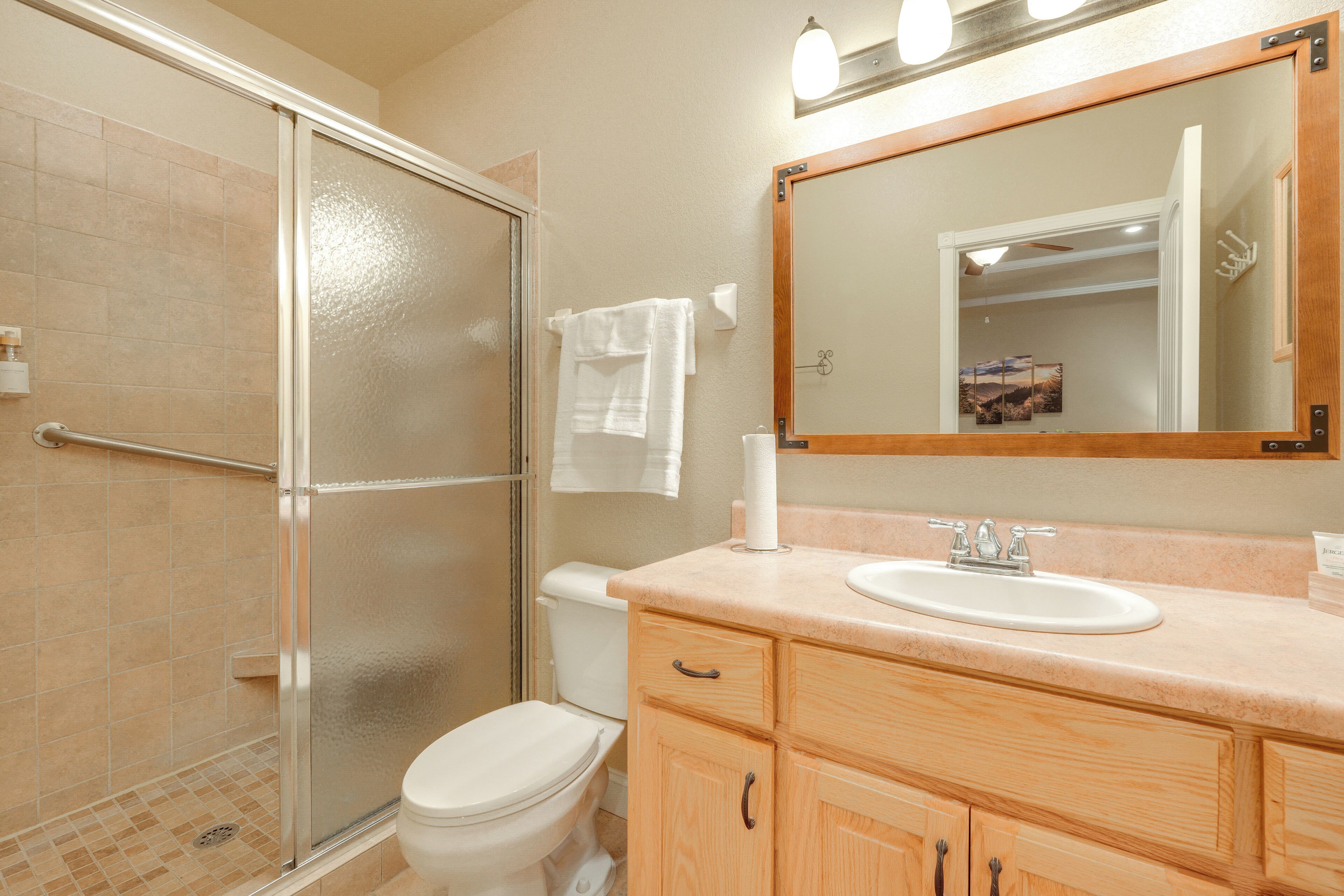 A bathroom with a glass shower enclosure, a toilet, a sink with a mirror above it, and wooden cabinets.