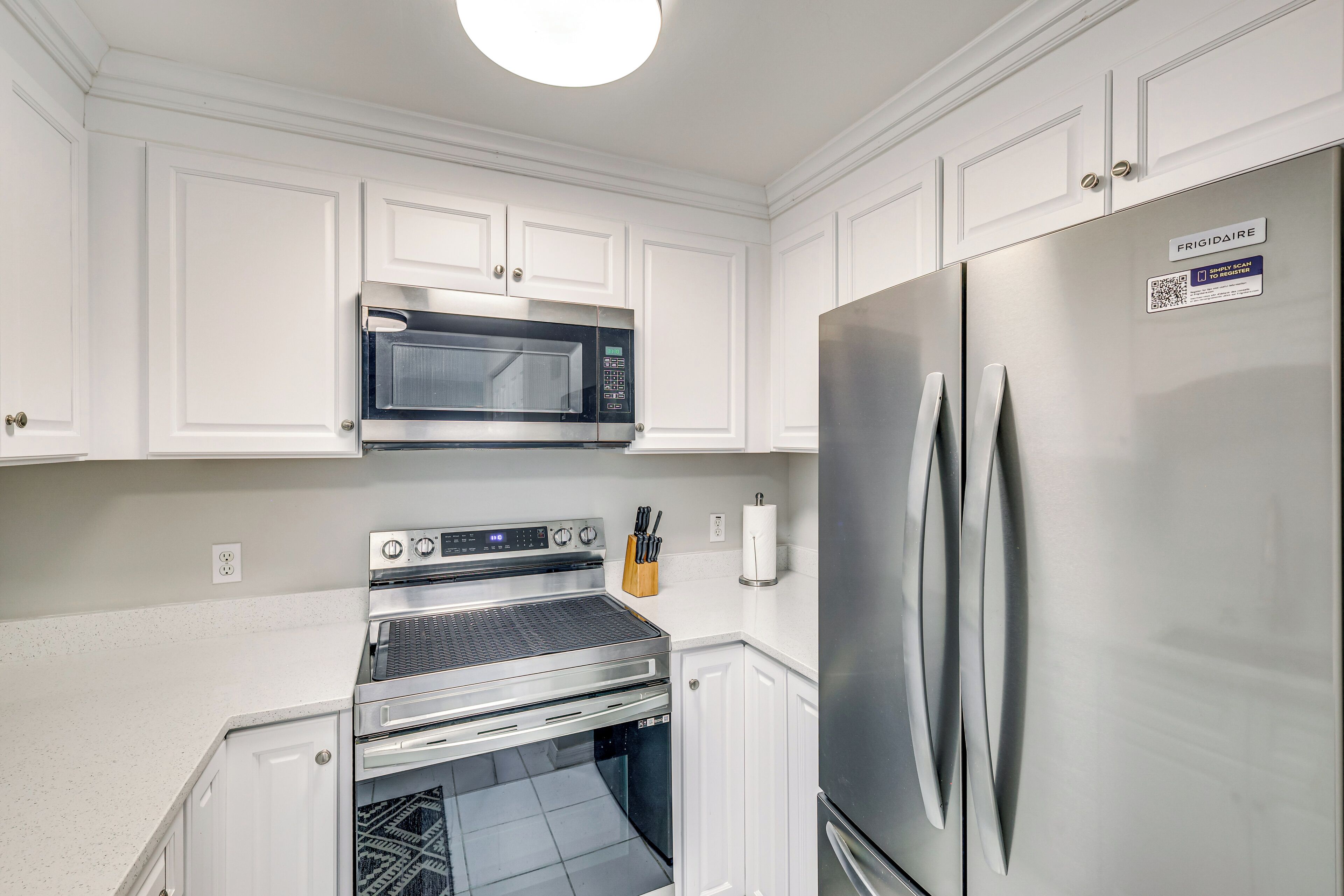 A modern kitchen with white cabinetry, a stainless steel refrigerator, a built-in oven, and a microwave.