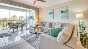 Ein geräumiges Wohnzimmer mit Sofa, Couchtisch und Sesseln, ein Balkon mit Aussicht und einem Deckenventilator.