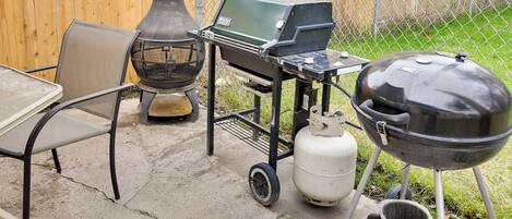 Een achtertuin met een draagbare barbecue, een gasfles en een tafel met stoelen.