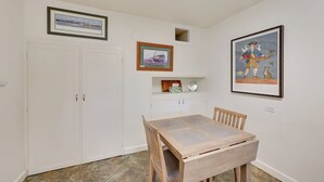 A dining area with a wooden table and chairs, white walls, and framed artwork.