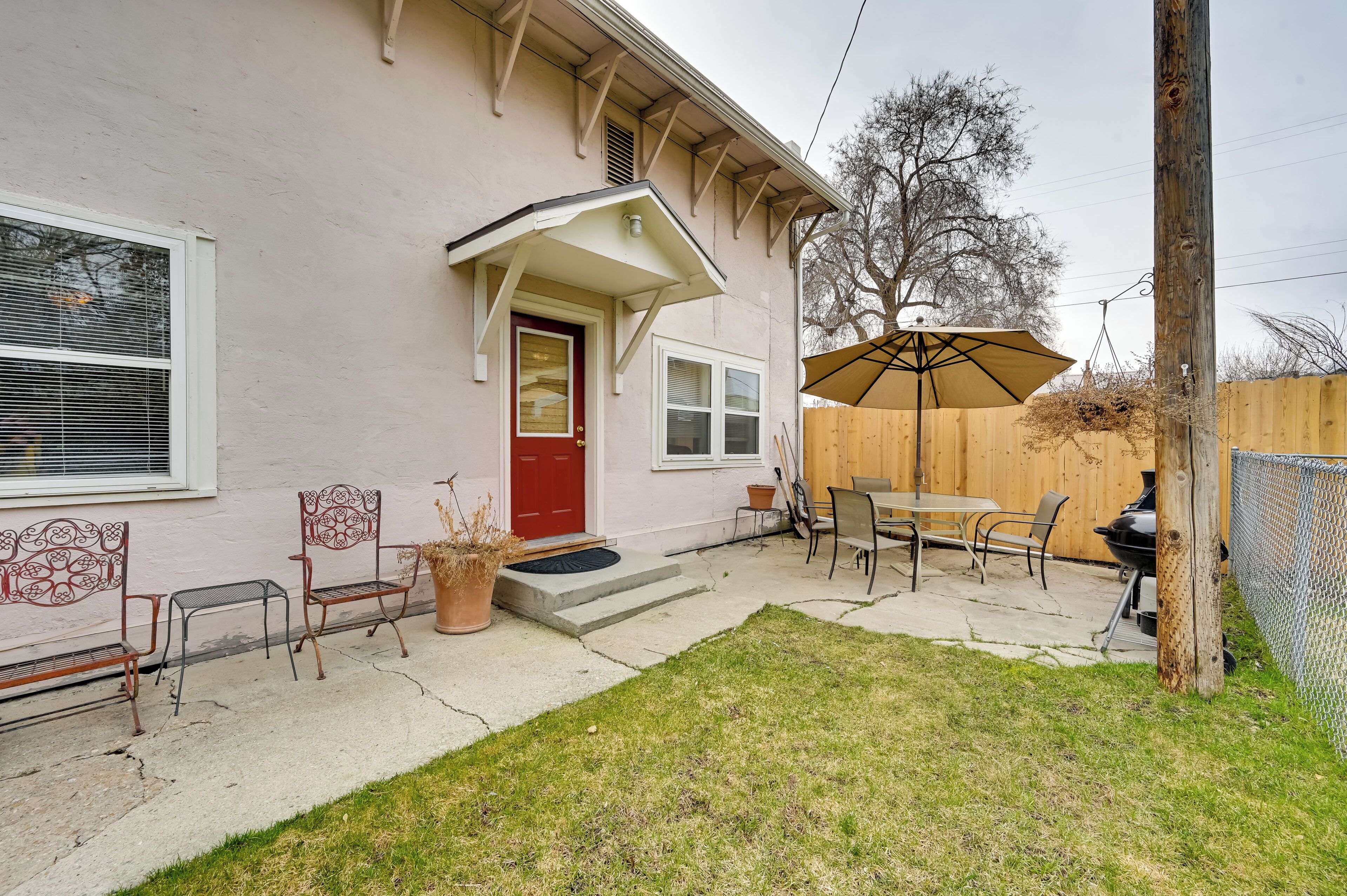 A house with a red door, a covered patio with a table and chairs, and a wooden fence in the background.