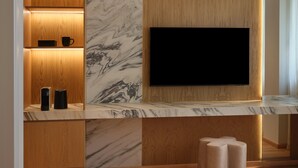 A modern interior with a flat-screen TV mounted on a marble wall, wooden shelving, and a built-in speaker system. - Nur City Suites (Athens)
