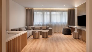 A modern living room with a sectional sofa, ottomans, a wooden accent wall, and a large flat-screen TV. - Nur City Suites (Athens)