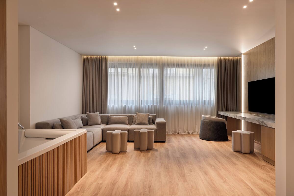 Ein modernes Wohnzimmer mit einer Eckcouch, Poufs, einer Wandvertäfelung aus Holz und einem großen Flachbildfernseher.