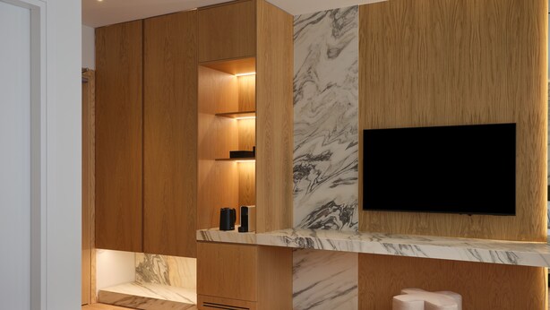 A modern bedroom with a wooden wardrobe, a marble accent wall, a flat-screen TV mounted on the wall, and a bedside table with two cushions. - Nur City Suites (Athens)